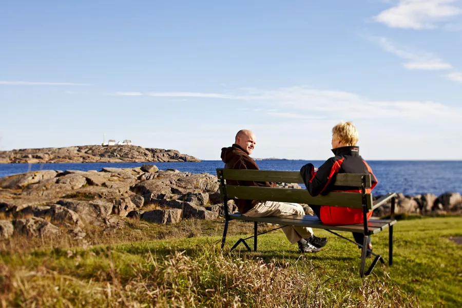 En mann og en kvinne sitter på en benk ute ved havet
