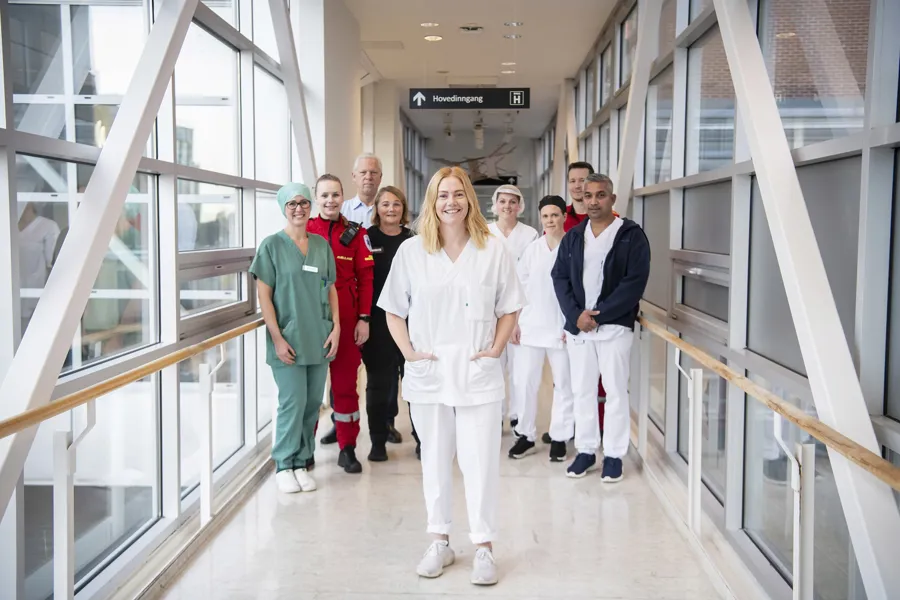 En gruppe ansatte fra ulike yrker står sammen og smiler mot kamera i en gang