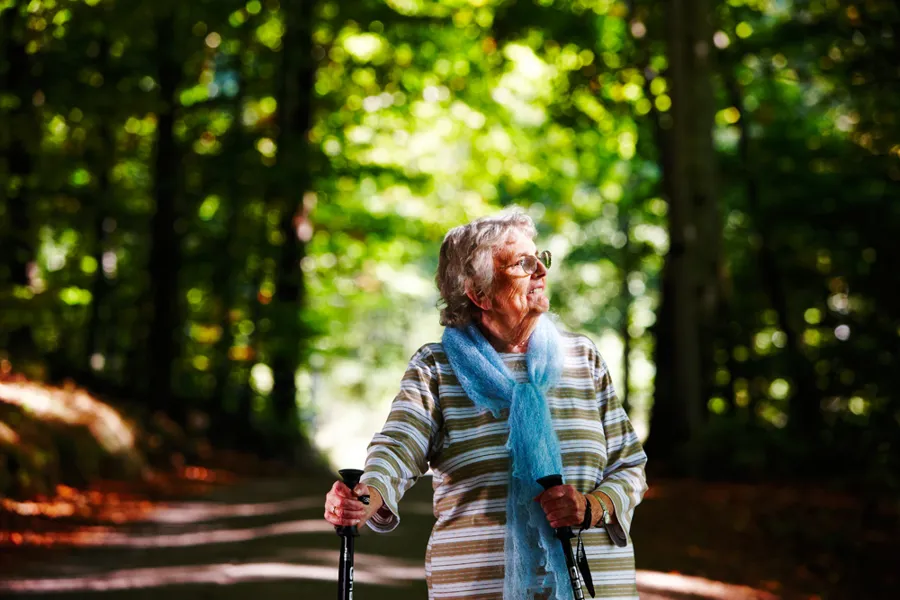 En eldre kvinne med gåstaver går på en sti i en skog