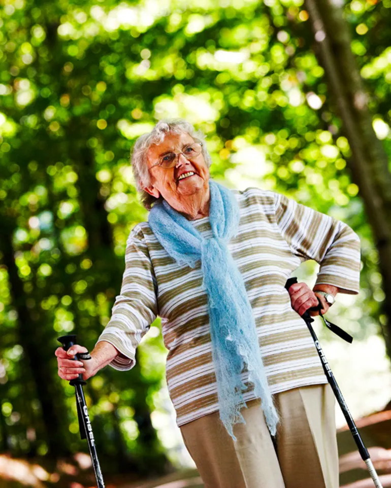 En eldre kvinne med gåstaver går tur på en sti i skogen