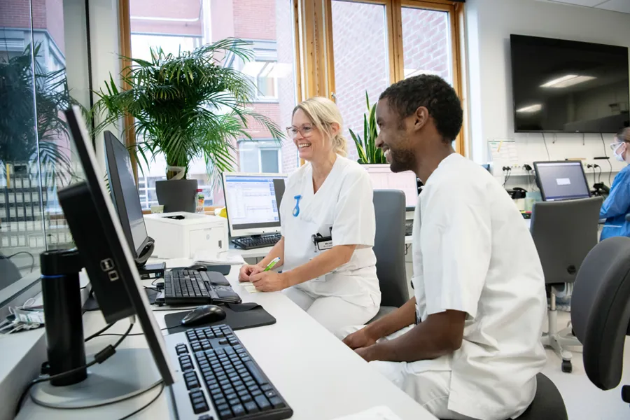En mann og en kvinne i hvitt arbeidsantrekk på et kontor foran dataskjermer