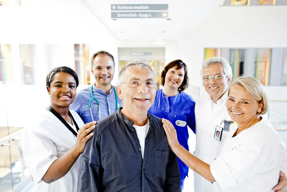 En gruppe helsepersonell står rundt en pasient og smiler til kamera