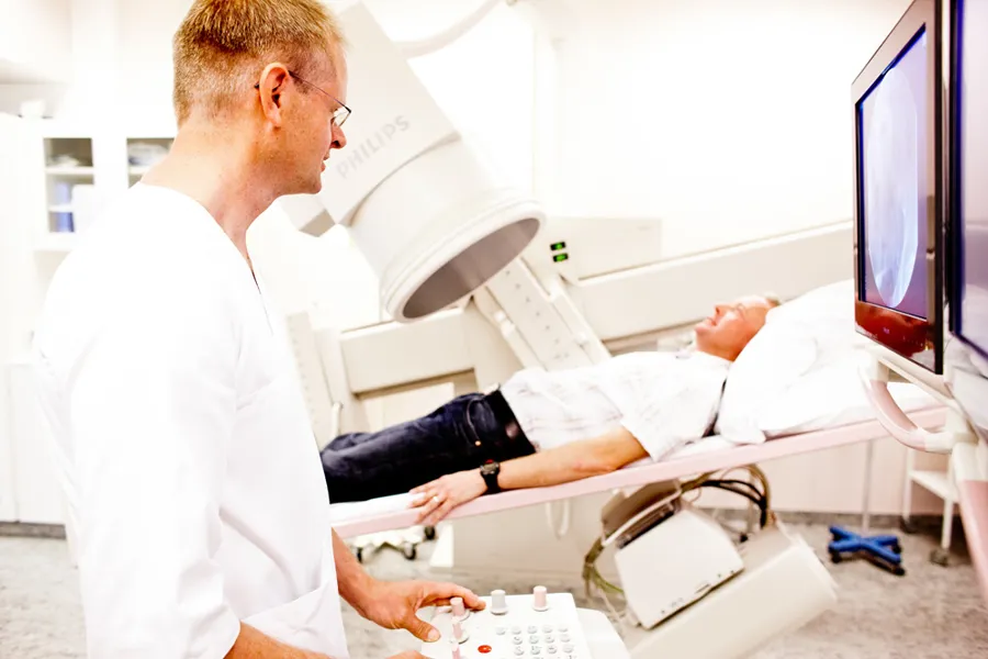 En mann i hvitt arbeidsantrekk gjør en radiologisk undersøkelse av en pasient som ligger på en benk