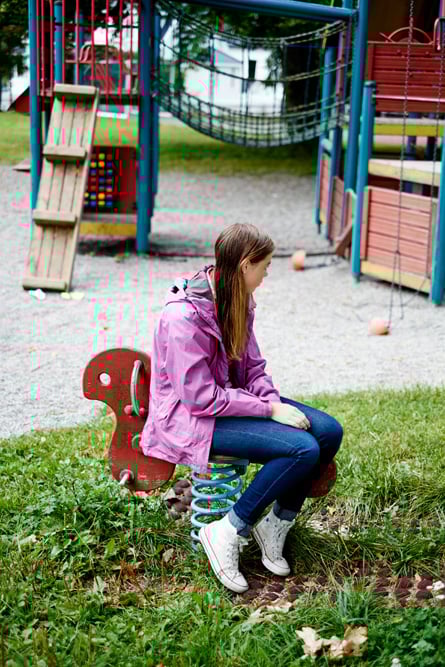 En ungdomsjente sitter på et lekeapparat på en lekeplass