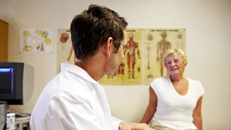 En lege sitter til venstre for en kvinne som sitter på en behandlingsbenk