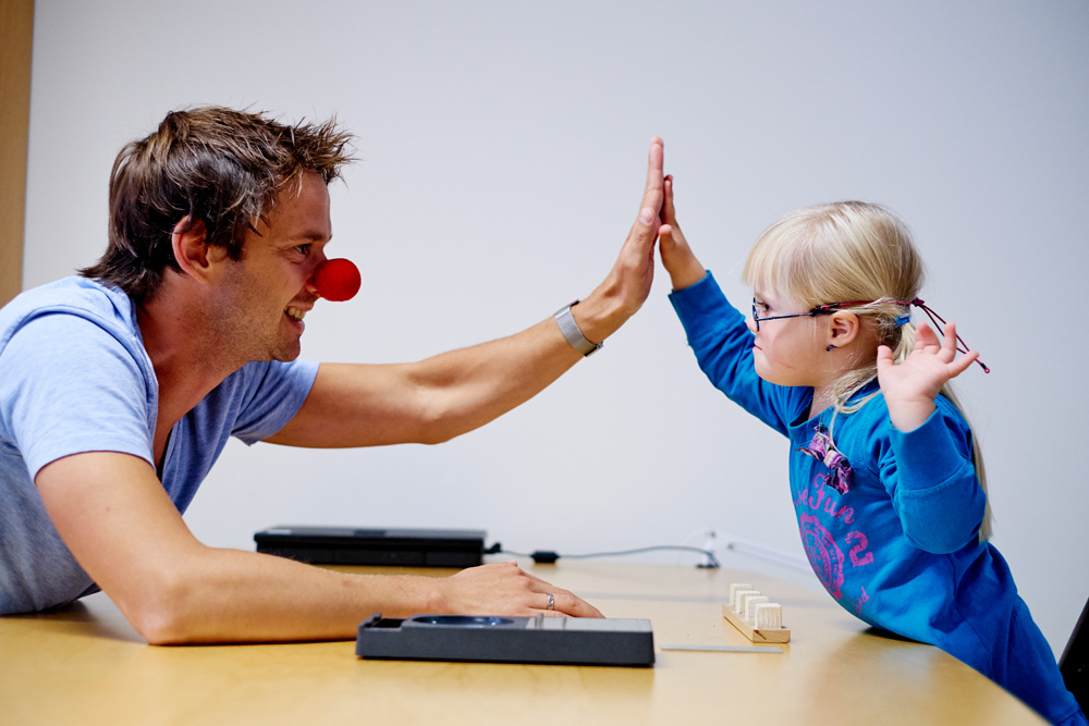 En mann med rød klovnenese og en ung jente gir hverandre en high five over et bord