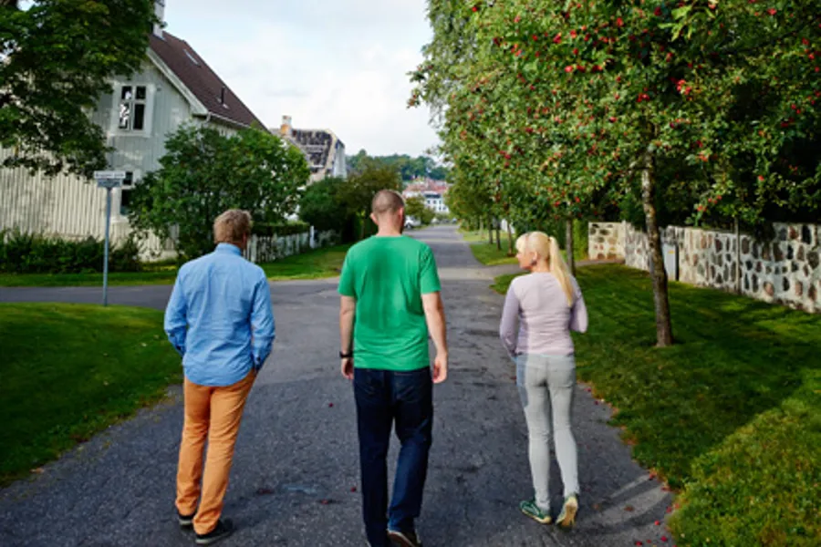 En gruppe mennesker som går nedover et fortau ved siden av et tre med røde blomster