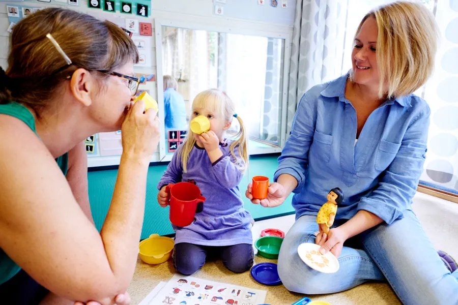 To kvinner og en liten jente sitter på gulvet og leker