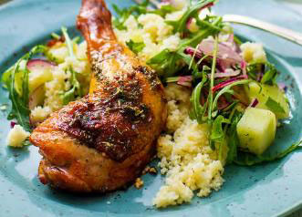 En tallerken med ovnsstekt kyllinglår servert med en stor porsjon grønnsaksrik salat med ruccola, rødløk og agurk, samt couscous som tilbehør.