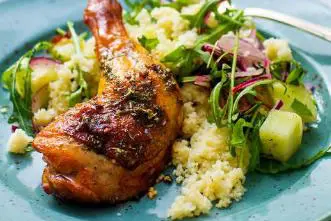En tallerken med ovnsstekt kyllinglår servert med en stor porsjon grønnsaksrik salat med ruccola, rødløk og agurk, samt couscous som tilbehør.
