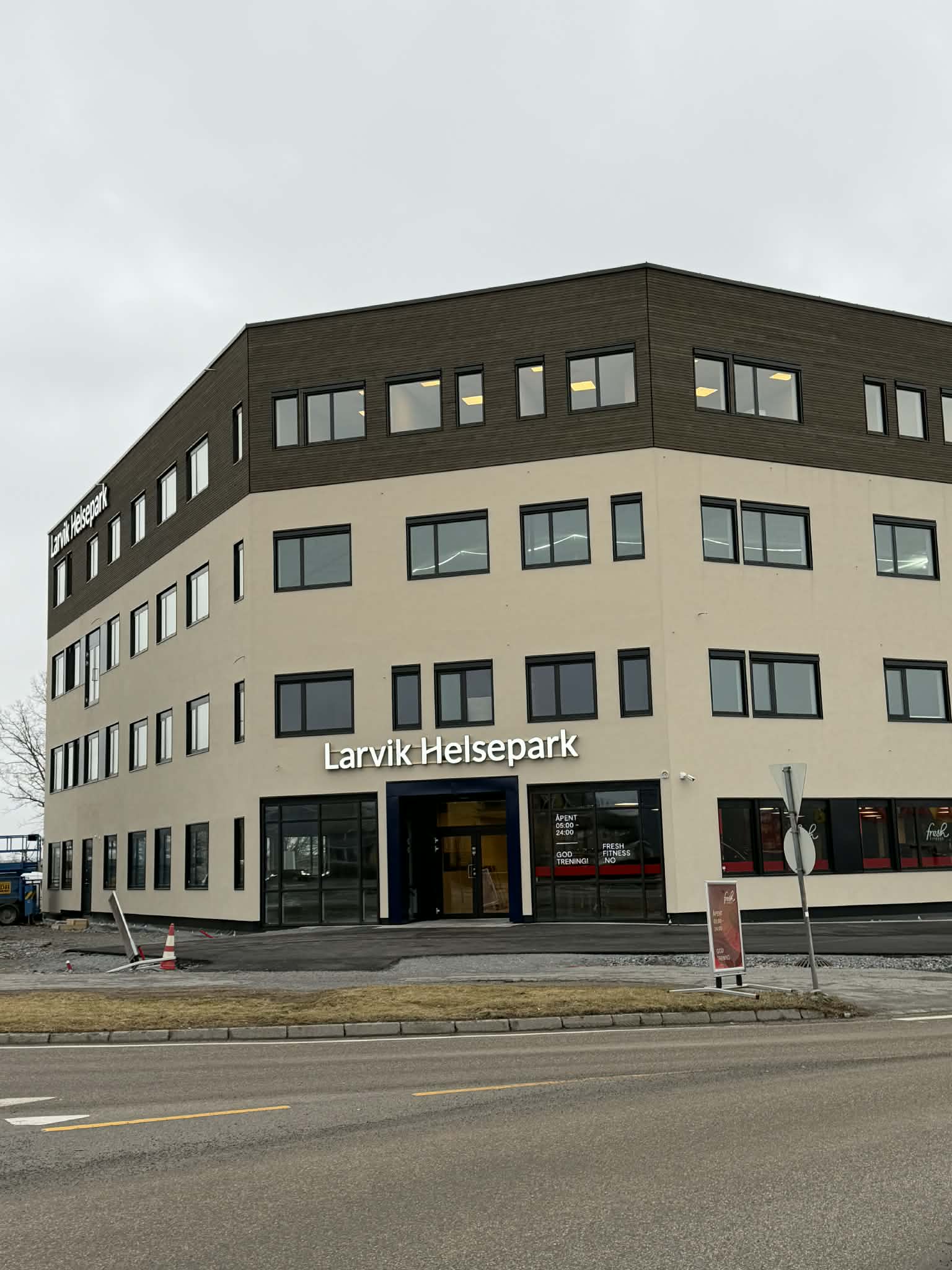 Fasadebilde av Larvik Helsepark, en lys, moderne kontorbygning med store vinduer og skilt med teksten «Larvik Helsepark» over hovedinngangen. Bildet er tatt fra gaten foran bygget på en overskyet dag.