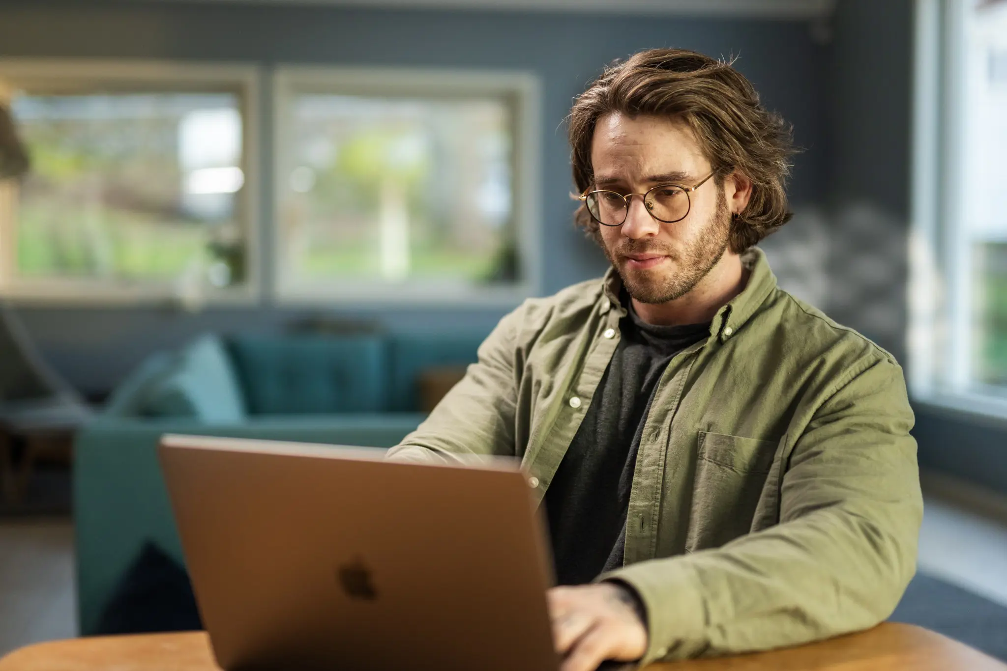 Ung mann med briller og bekymret mine i ansiktet sitter ved bord og ser på skjermen til en laptop.