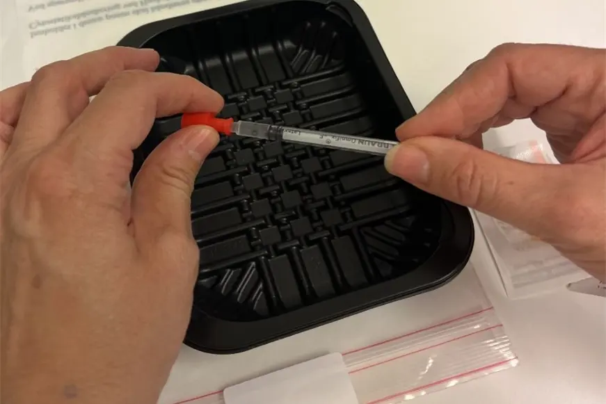 Nærbilde av en som skrur av den røde proppen på sprøyten