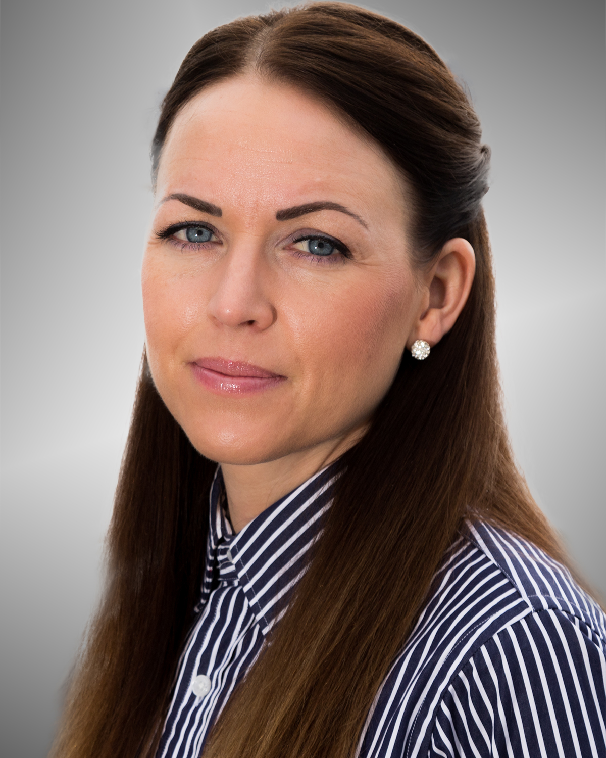 Portrettfoto av en voksen person med langt, mørkt hår bakover, iført stripet skjorte, fotografert mot en grå, nøytral bakgrunn.