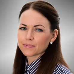 Portrettfoto av en voksen person med langt, mørkt hår bakover, iført stripet skjorte, fotografert mot en grå, nøytral bakgrunn.