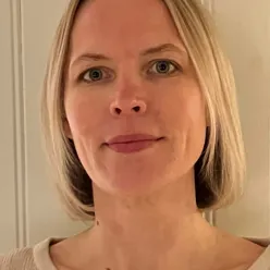 Portrettfoto av en voksen person med lyst, skulderlangt hår, iført lys genser, fotografert innendørs mot en lys bakgrunn.