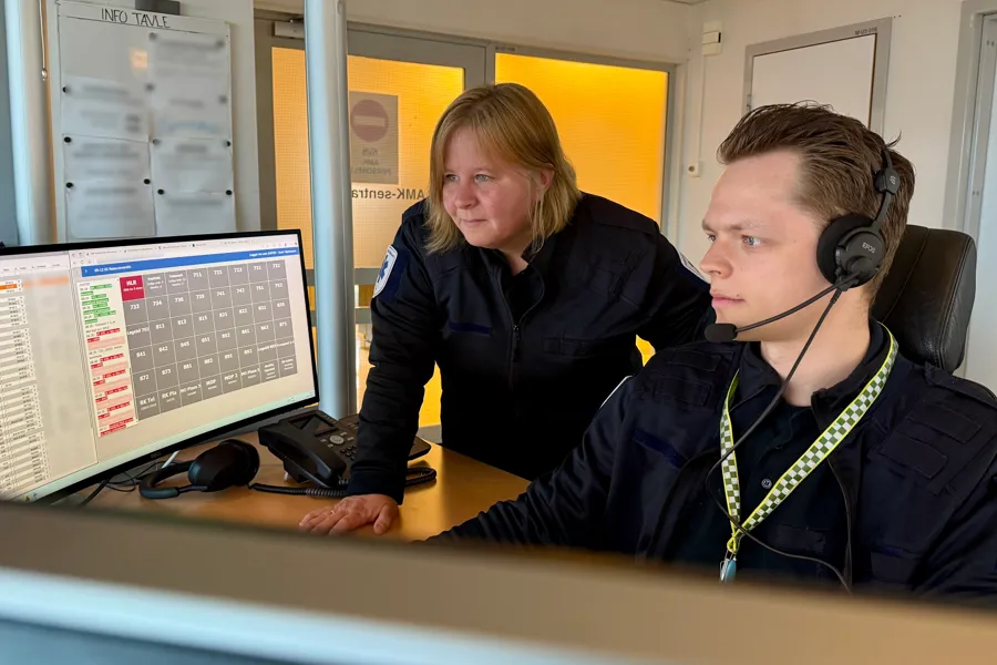 Mann sitter med headsett og leser tallskjemaer på skjermene foran seg. Ved siden av står en kvinne bøyd og ser på skjermene.