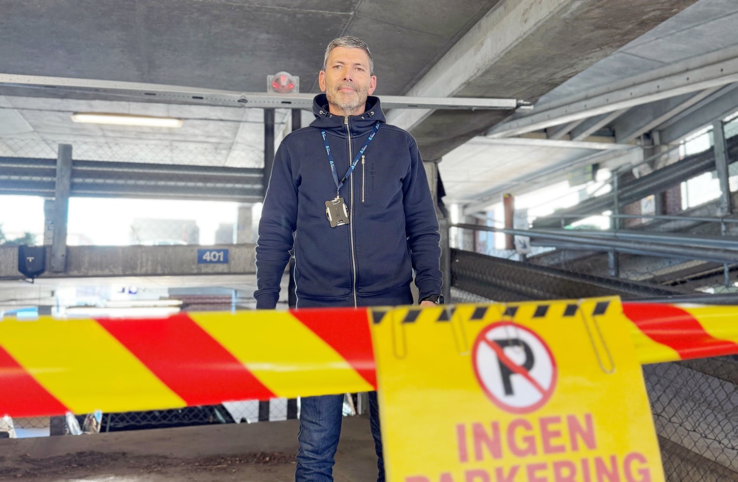 En mann står i et parkeringshus foran en sperring med «Ingen parkering»-skilt og avsperringsbånd.