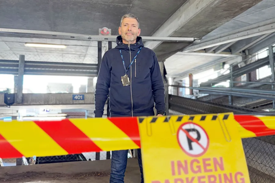 En mann står i et parkeringshus foran en sperring med «Ingen parkering»-skilt og avsperringsbånd.