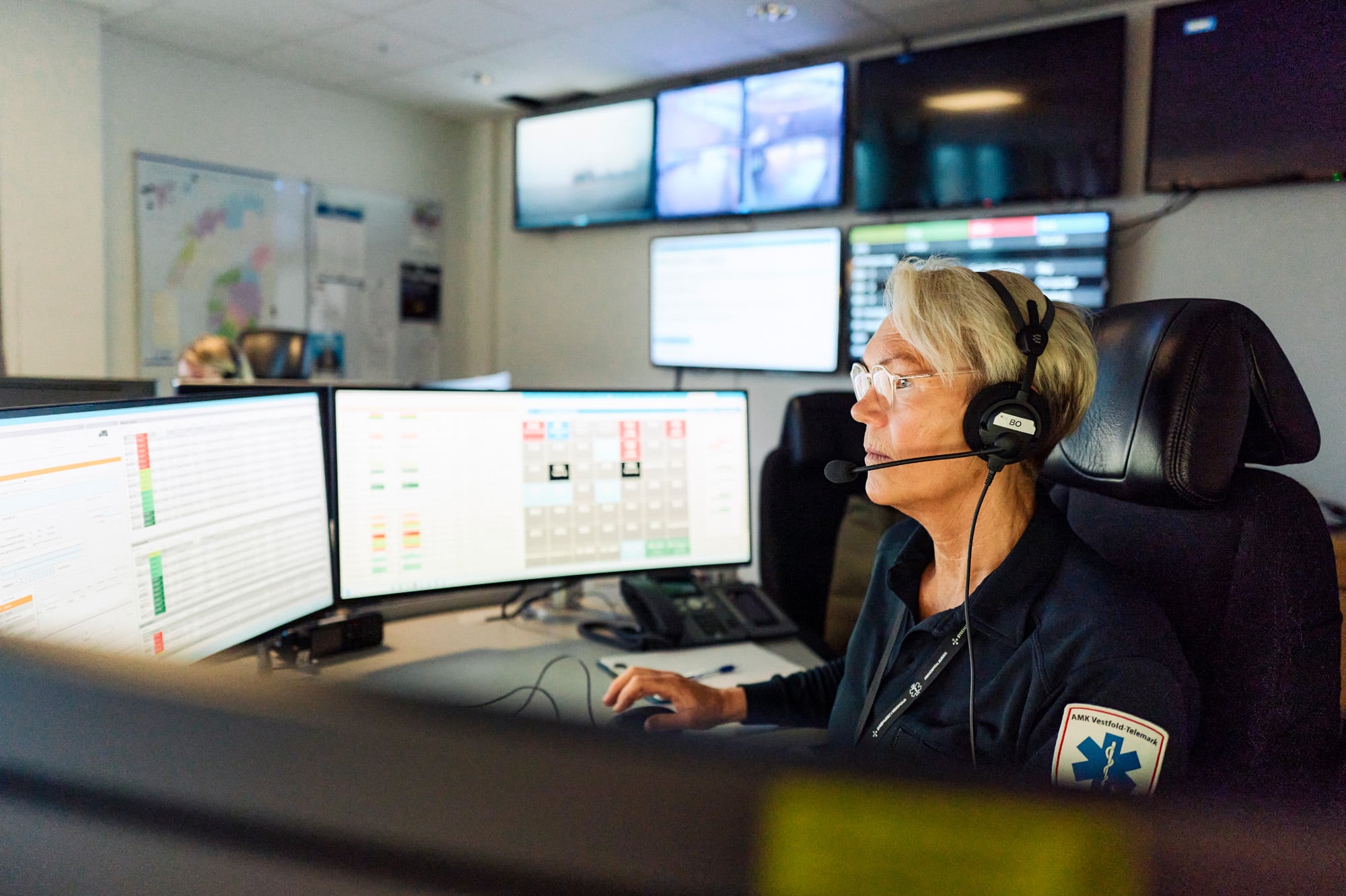 AMK-operatør med headset sitter i AMK-sentralen foran PC-skjermer