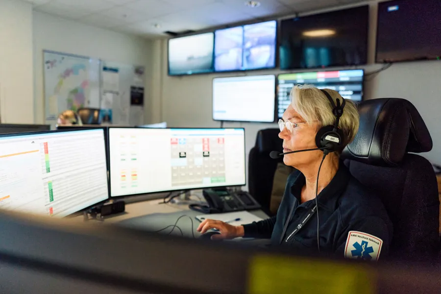 AMK-operatør med headset sitter i AMK-sentralen foran PC-skjermer