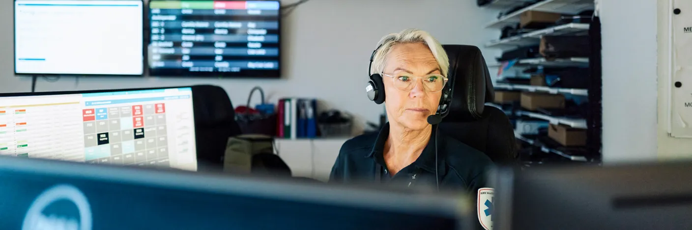 AMK-operatør med headset sitter i AMK-sentralen foran PC-skjermer
