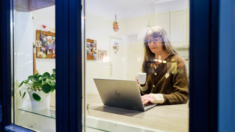 En person som sitter ved et skrivebord med en laptop og en kopp