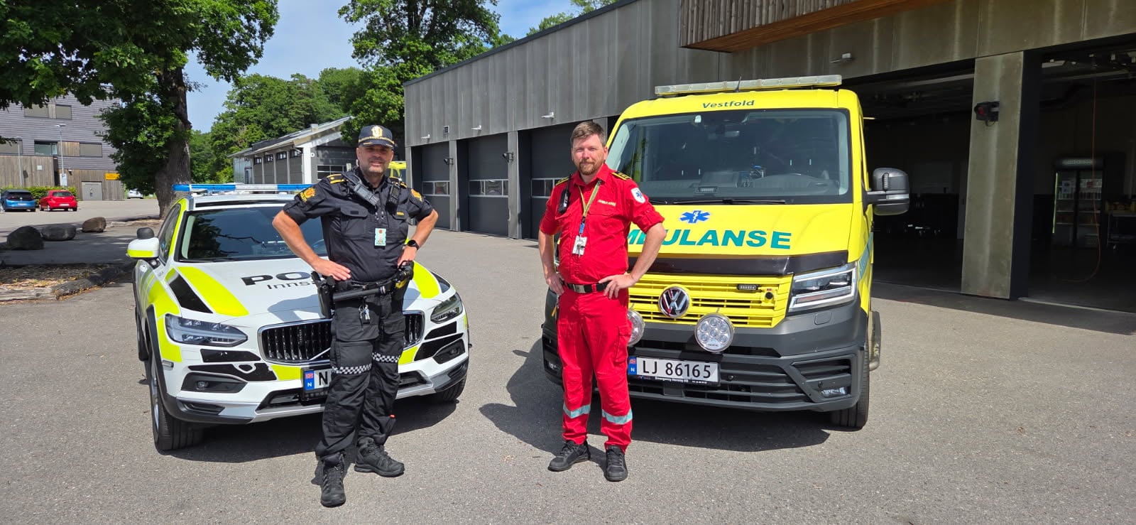 To menn i henholdsvis politiuniform og ambulanseuniform står foran politibil og ambulanse