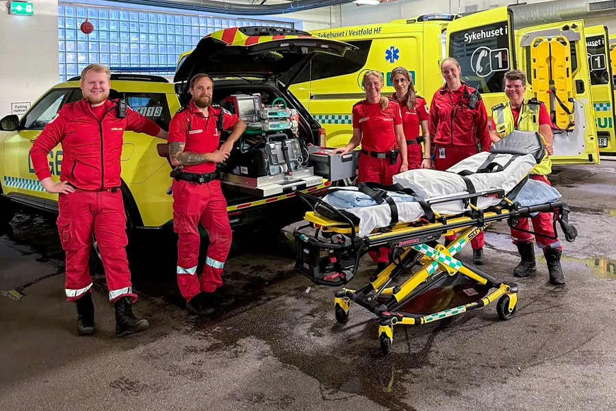 En gruppe mennesker i røde jumpsuits som står ved siden av en gul og svart maskin