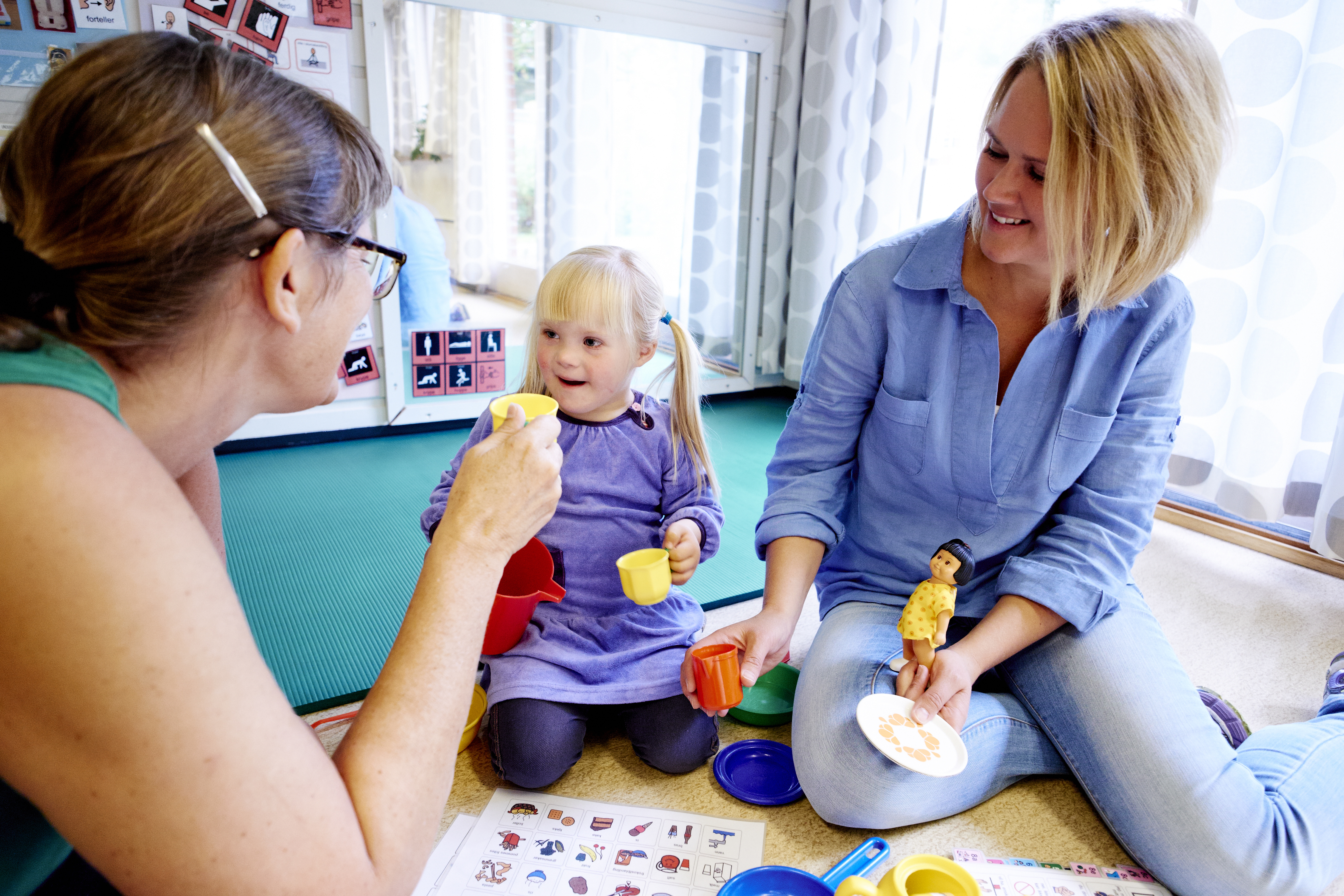 To kvinner og et barn sitter på gulvet og leker