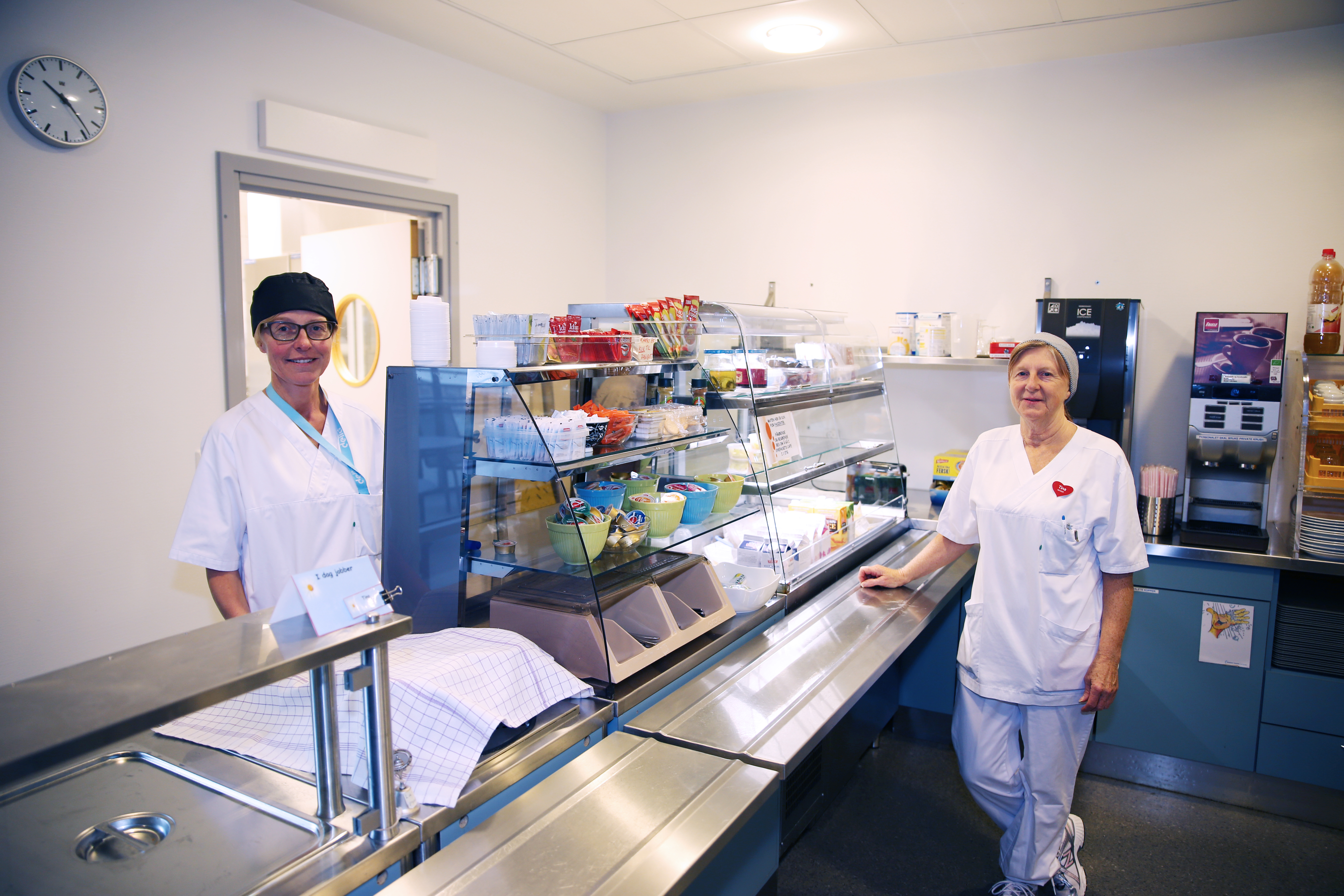 To kvinner i hvitt arbeidsantrekk står i en kantine
