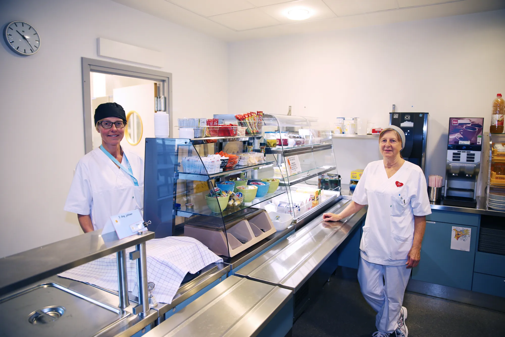To kvinner i hvitt arbeidsantrekk står i en kantine