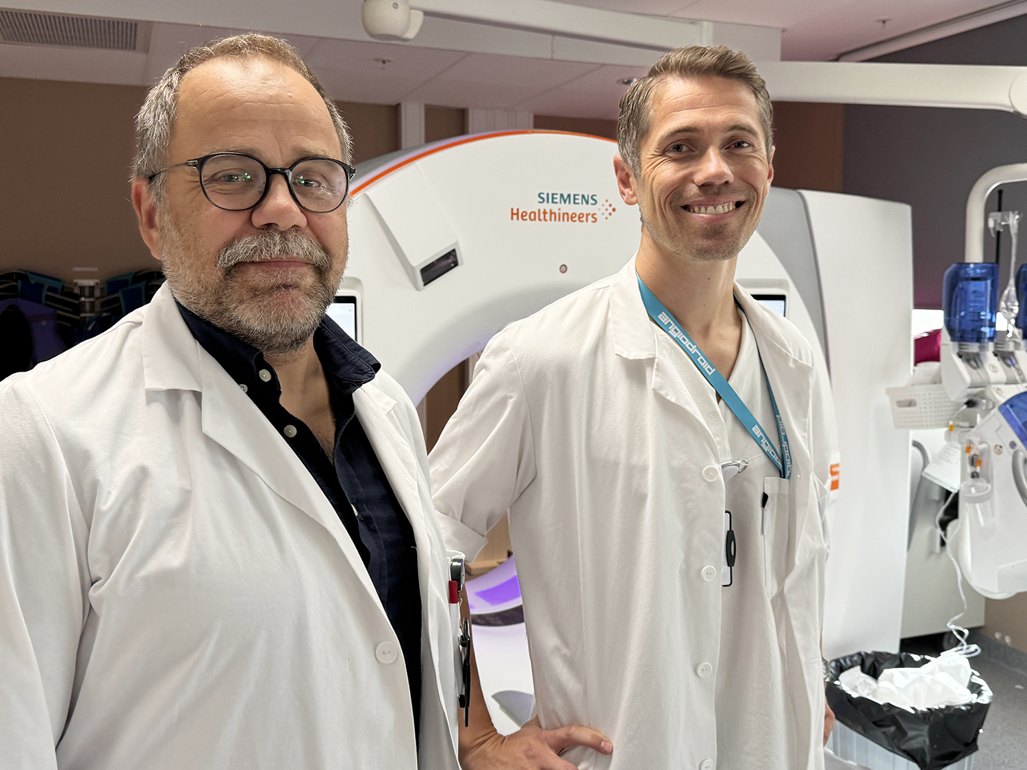 To helsearbeidere i hvite frakker står foran en Siemens Healthineers CT‑maskin i et klinisk rom.