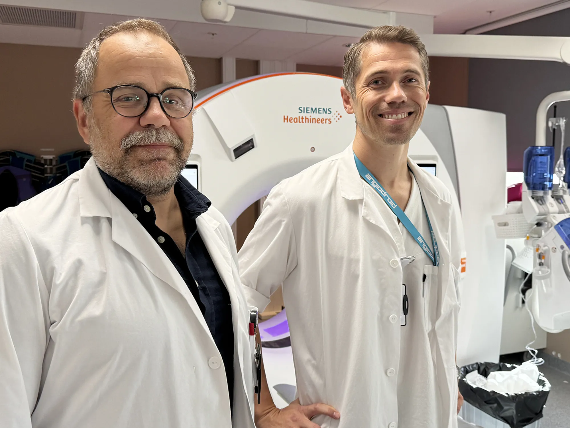 To helsearbeidere i hvite frakker står foran en Siemens Healthineers CT‑maskin i et klinisk rom.