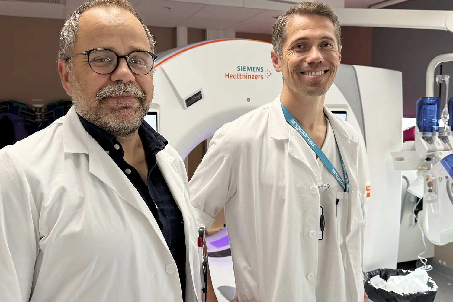 To helsearbeidere i hvite frakker står foran en Siemens Healthineers CT‑maskin i et klinisk rom.