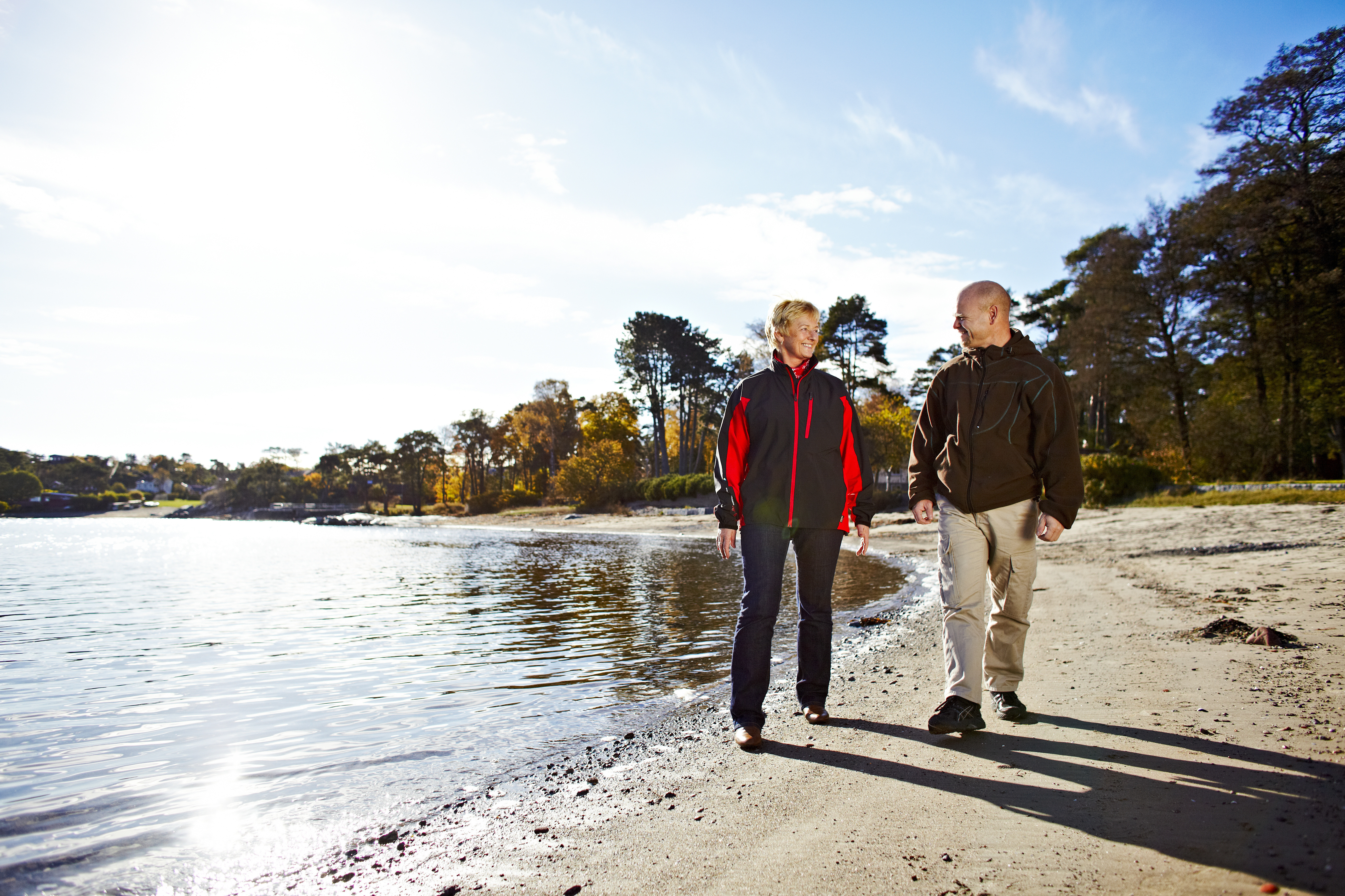 En kvinne og en mann går tur på en strand i fint vær
