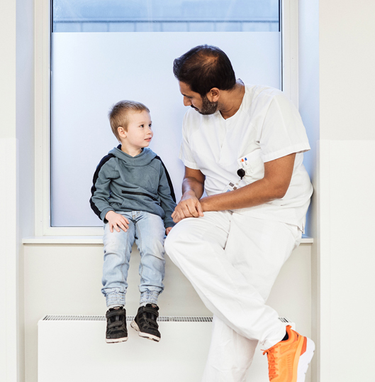 En lege i hvitt arbeidsantrekk og en gutt sitter i en vinduskarm