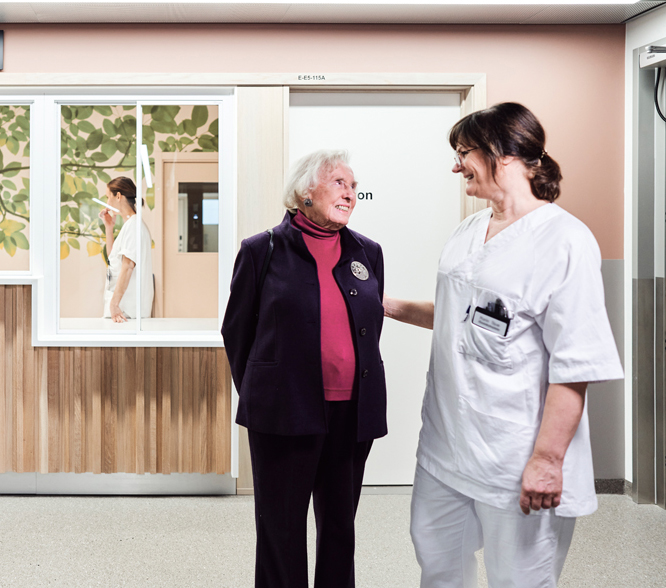 En eldre kvinne og en sykepleier i hvitt arbeidsantrekk ser på hverandre