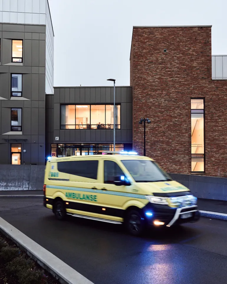 En gul ambulanse med blålys kjører utenfor sykehuset