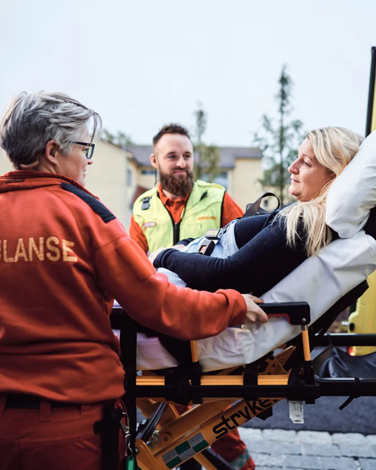 To ambulansearbeidere triller pasient på båre ut av ambulanse