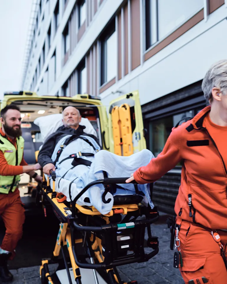 To ambulansearbeidere triller pasient på båre ut av ambulanse