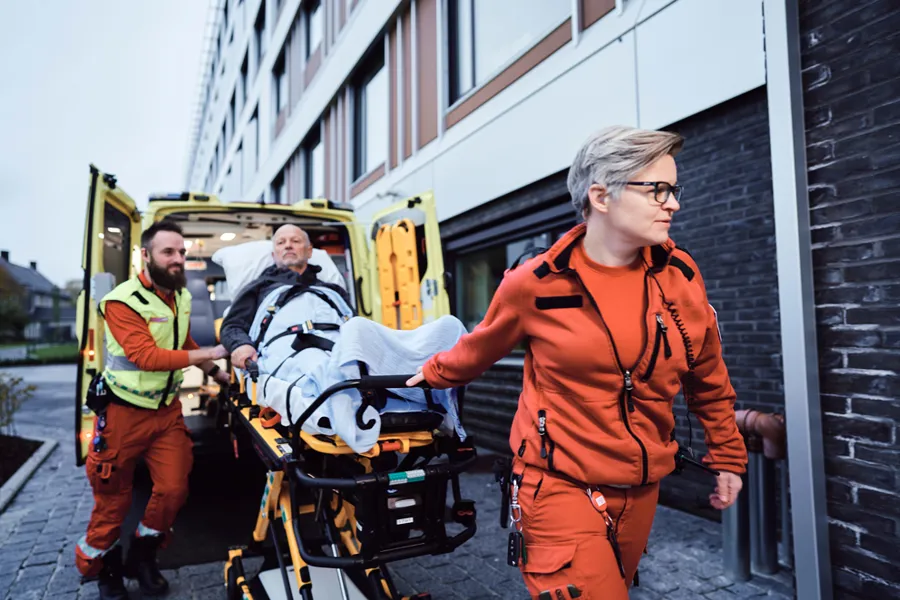 To ambulansearbeidere triller pasient på båre ut av ambulanse