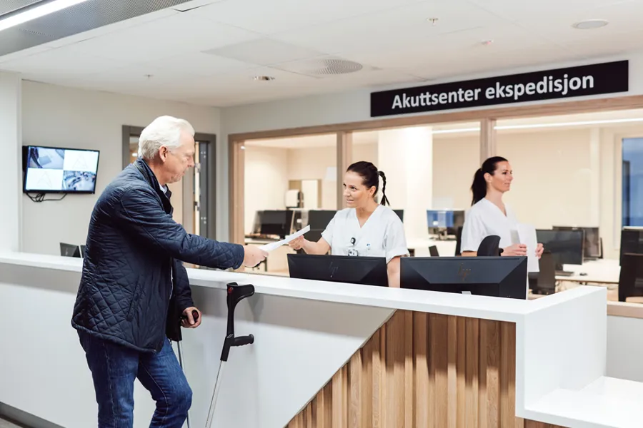 En mann på krykker snakker med en sykepleier i resepsjonen i akuttsenteret