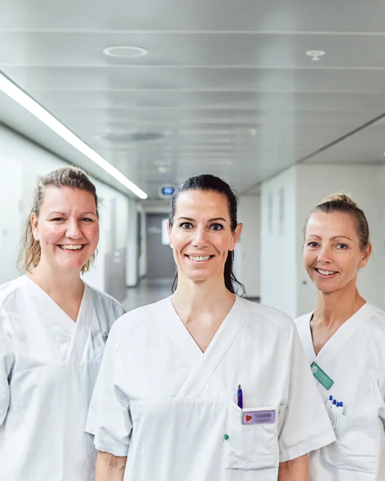 Tre smilende, kvinnelige sykepleiere i hvitt arbeidsantrekk