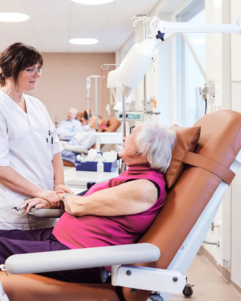 Sykepleier snakker med pasient som sitter i en stol