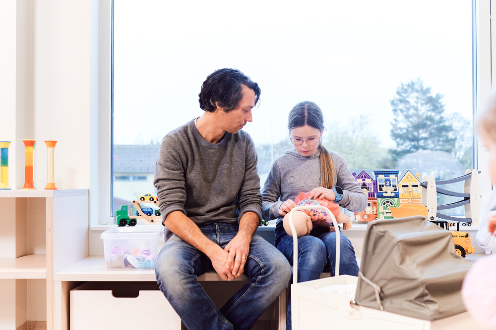 En mann og et barn leker med en dukke på lekerommet