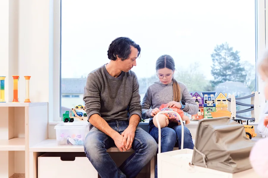 En mann og et barn leker med en dukke på lekerommet