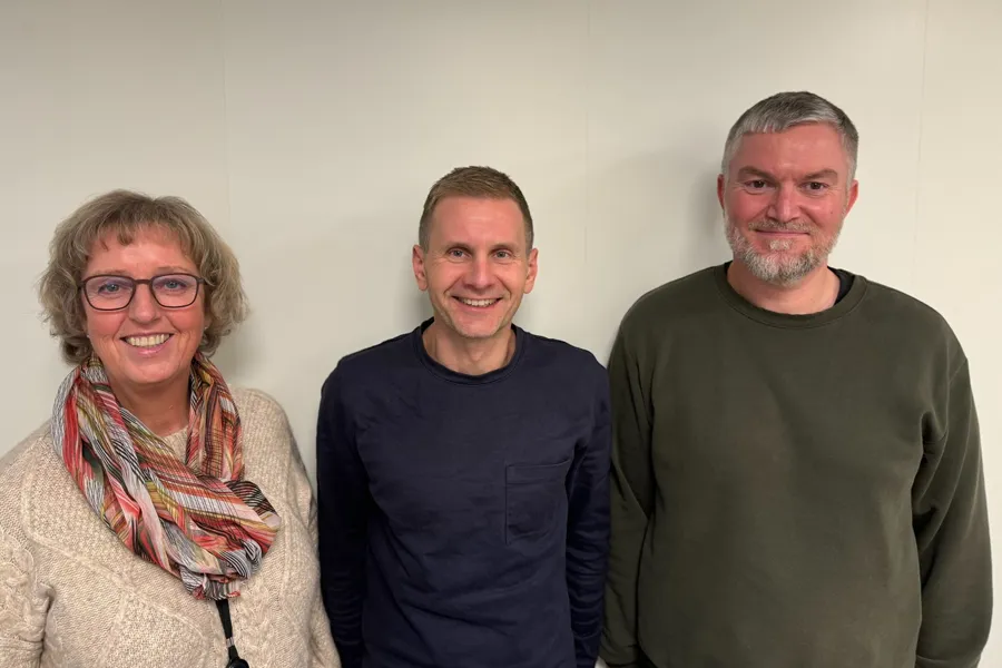 En kvinne og to menn som smiler